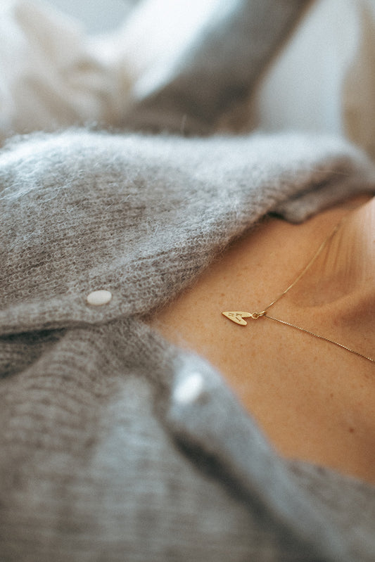 Close-up of a person wearing a gray sweater with a gold necklace featuring a heart pendant.